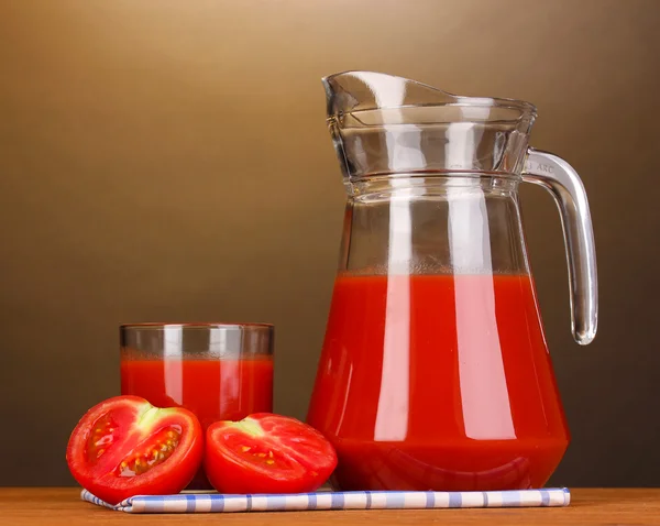 Tomatensap in werper en glas op houten tafel op bruine achtergrond — Stockfoto