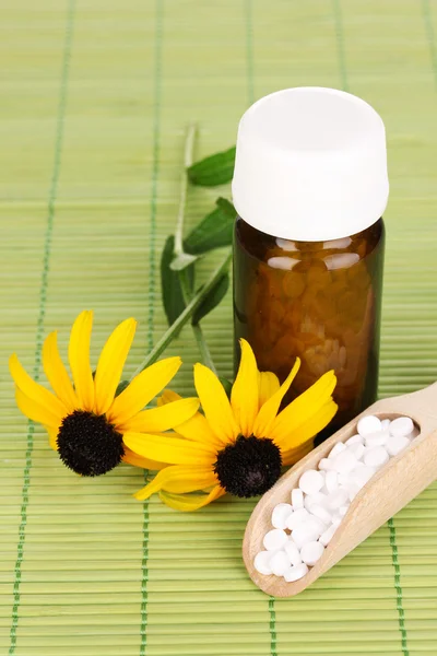 Medicine bottle with tablets and flowers on bamboo mat — Stock Photo, Image