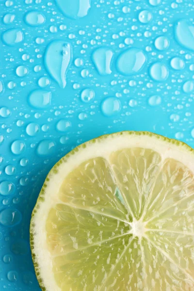 Slice of lime with drop on blue background — Stock Photo, Image