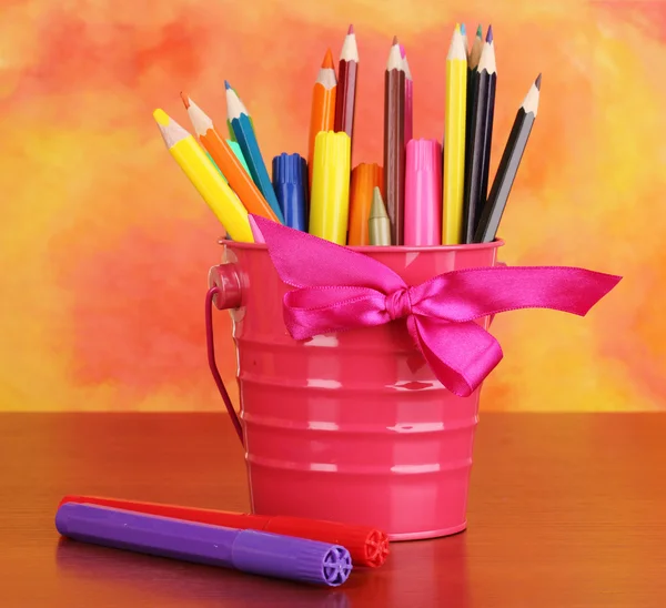 Colorful pencils and felt-tip pens in pink pail on color background — Stock Photo, Image