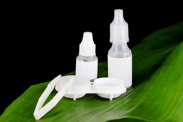 Eye drops and lenses on leaf on black background — Stock Photo, Image