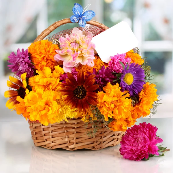 Beautiful bouquet of bright flowers in basket with paper note on white tabl — Stock Photo, Image
