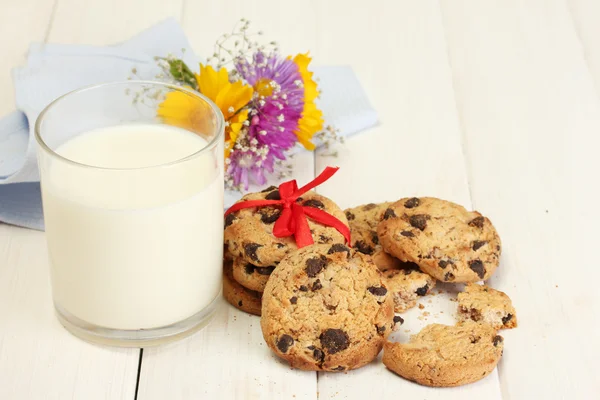 Vaso de leche, galletas de chispas de chocolate con cinta roja y flores silvestres en w — Foto de Stock