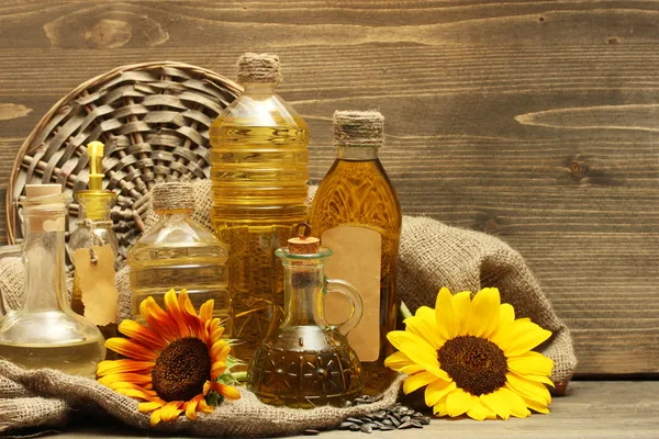 Oil in bottles, sunflowers and seeds, on wooden background — Stock Photo, Image