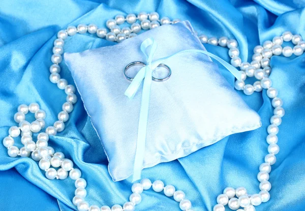 Anneaux de mariage sur oreiller en satin sur fond de tissu bleu — Photo