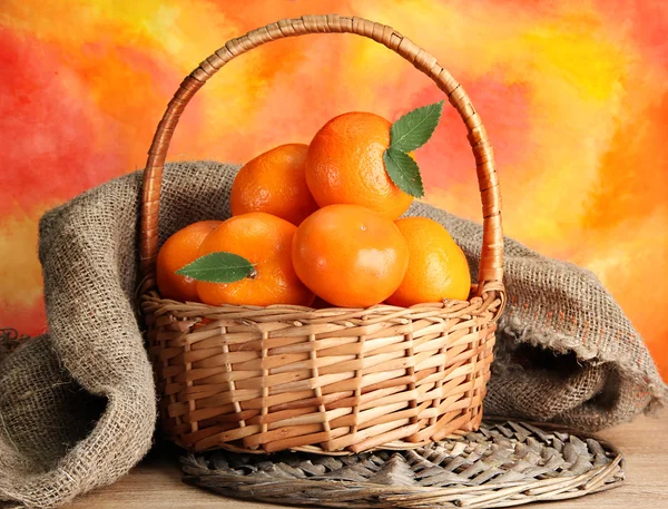 Tangerines with leaves in a beautiful basket, on wooden table on orange bac — Stock Photo, Image