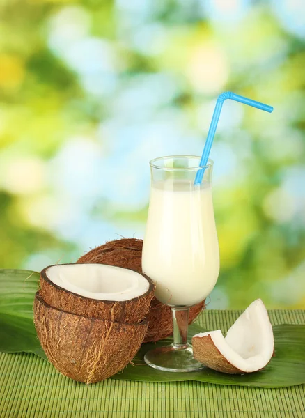 Glass of coconut milk and coconuts on green background close-up — Stock Photo, Image