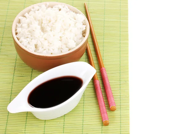 Bowl of rice and chopsticks on bamboo mat isolated on white — Stock Photo, Image