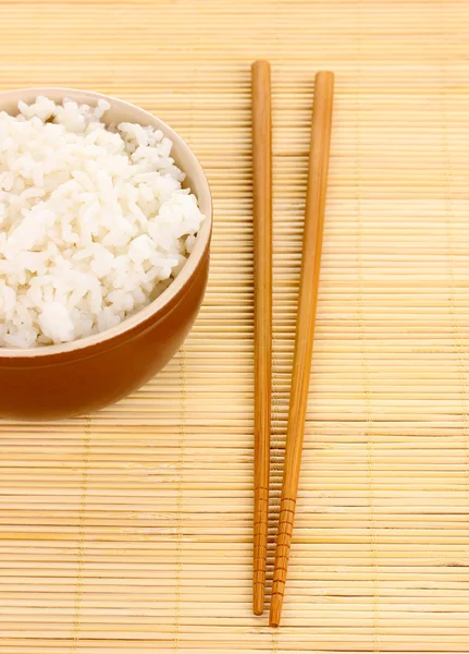 Tigela de arroz e pauzinhos em esteira de bambu — Fotografia de Stock