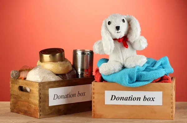Donation boxes with clothing and food on red background close-up — Stock Photo, Image