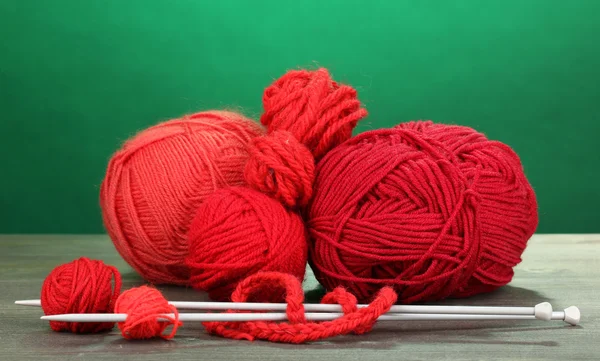 Red knittings yarns on wooden table on green background — Stock Photo, Image