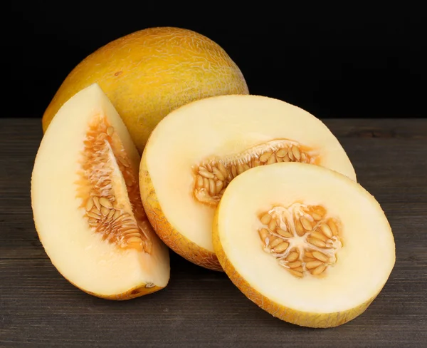 Cut ripe melons on wooden table on black background — Stock Photo, Image