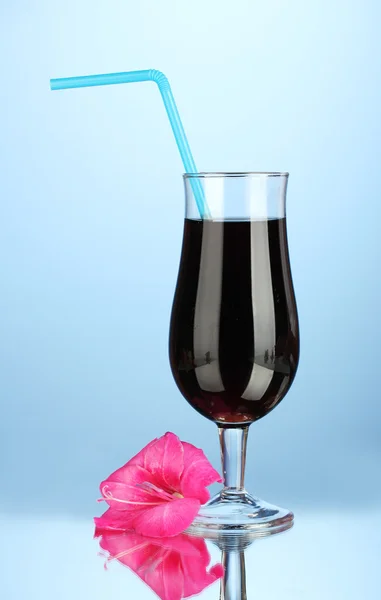 Glass with cocktail and gladiolus bud on blue background close-up — Stock Photo, Image