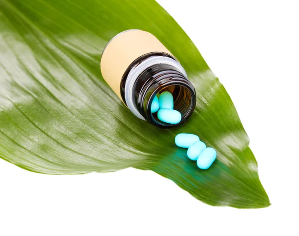 Tabletten op groene blad met fles geïsoleerd op wit — Stockfoto