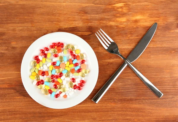 Un montón de pastillas en un plato con cuchillo y tenedor sobre fondo de madera primer plano —  Fotos de Stock