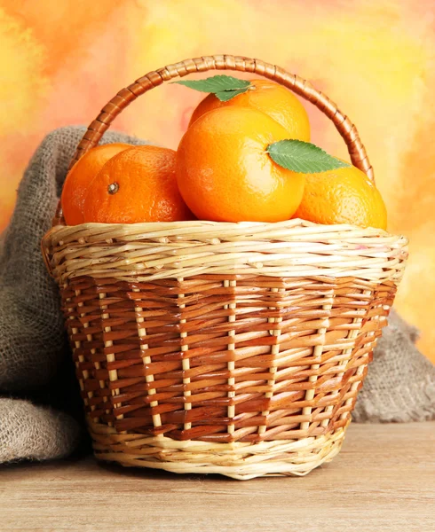Mandarinen mit Blättern in einem schönen Korb, auf einem Holztisch auf orangefarbenem Bac — Stockfoto