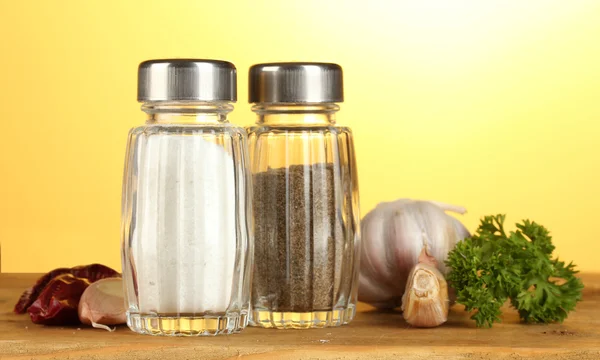 Salt and pepper mills, garlic and parsley on wooden table on yellow backgro — Stock Photo, Image