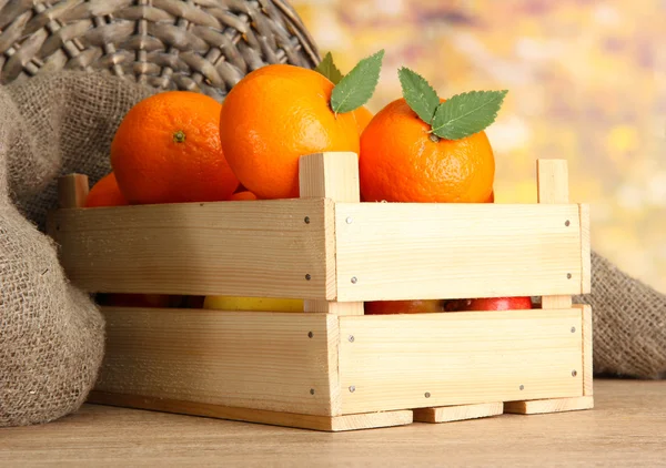Las mandarinas maduras sabrosas con las hojas en la caja de madera a la mesa sobre el fondo anaranjado —  Fotos de Stock