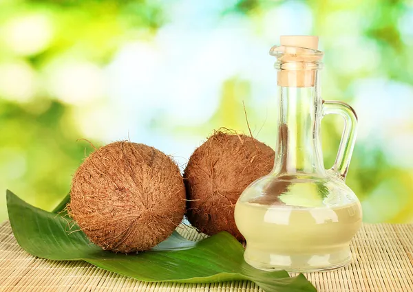 Decantador con aceite de coco y cocos sobre fondo verde —  Fotos de Stock
