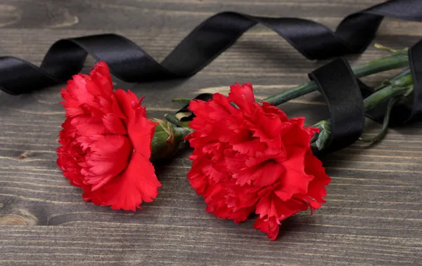 Carnations and black ribbon on grey wooden background — Stock Photo, Image