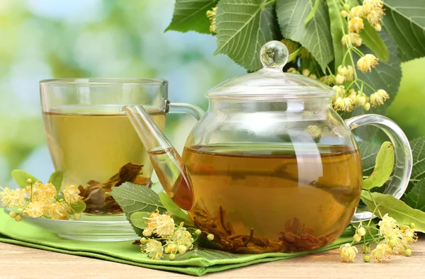 Tetera y taza con té de tilo y flores en la mesa de madera en el jardín —  Fotos de Stock