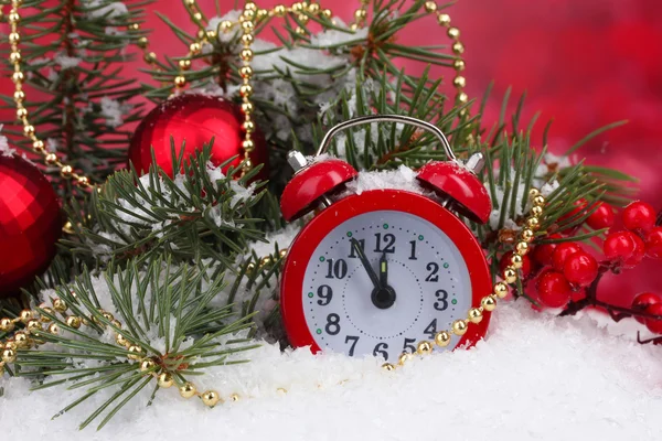 Grüner Weihnachtsbaum mit Spielzeug und Uhr im Schnee auf rot — Stockfoto