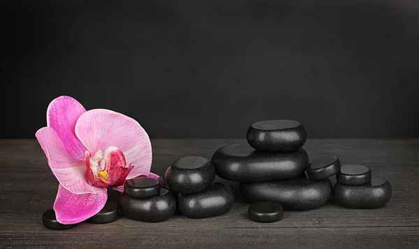 Piedras de spa con flor de orquídea sobre mesa de madera sobre fondo gris —  Fotos de Stock