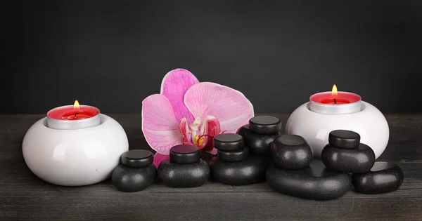 Pietre termali con fiore di orchidea e candele su tavolo di legno su sfondo grigio — Foto Stock