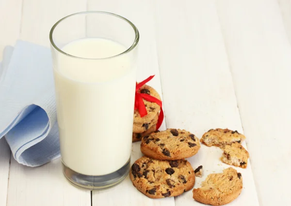 Glas melk en chocolade chips cookies met rood lint op houten tafel — Stockfoto