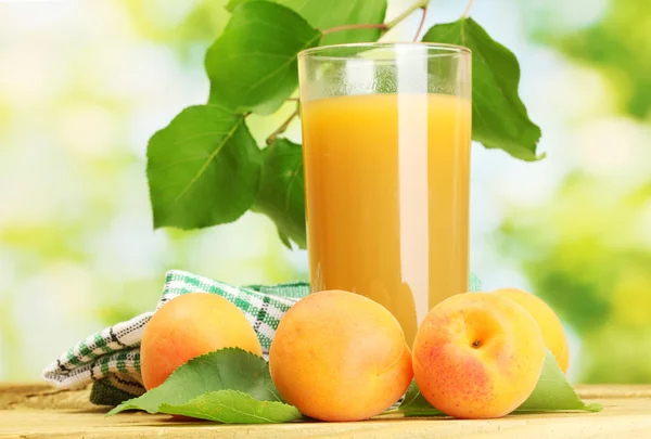 Glass of apricot juice and fresh apricots on wooden table on green backgrou — Stock Photo, Image