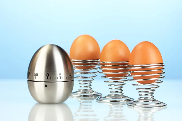 Temporizador de huevo y huevo en soporte de metal sobre fondo azul — Foto de Stock