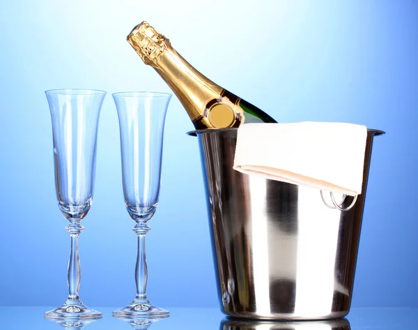 Champagne bottle in bucket with ice and glasses on blue background — Stock Photo, Image