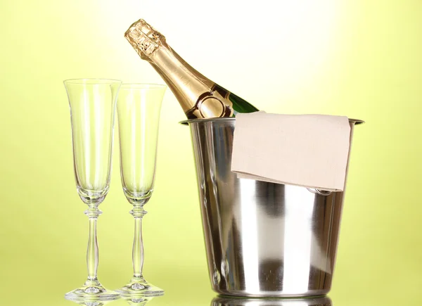 Champagne bottle in bucket with ice and glasses on green background — Stock Photo, Image