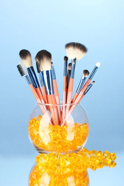 Pincéis de maquiagem em uma tigela com pedras no fundo azul — Fotografia de Stock