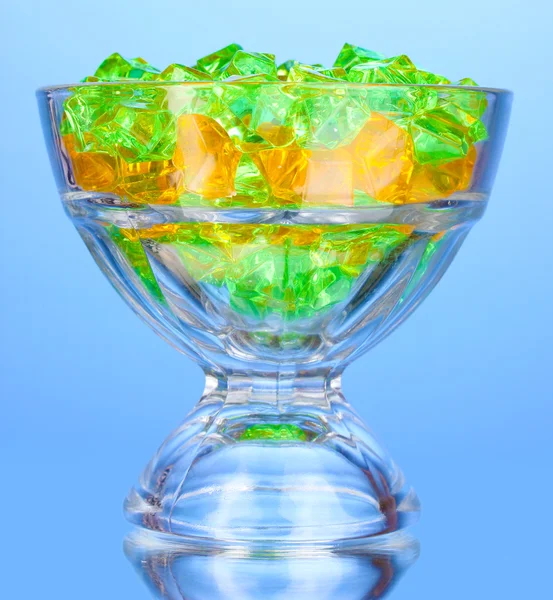 A glass with colorful decorative stones on blue background close-up — Stock Photo, Image