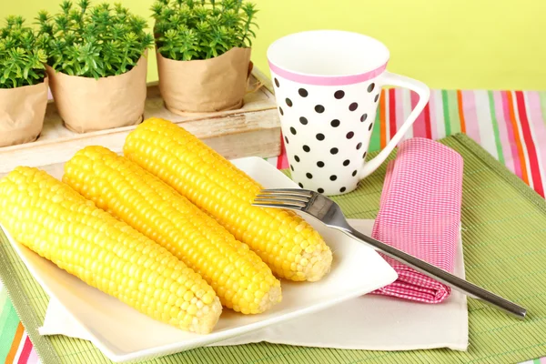 Gekochter Mais und eine Tasse auf grünem Hintergrund — Stockfoto