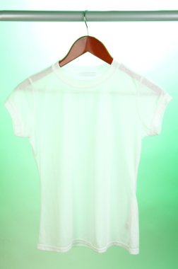 Askı üzerinde yeşil bir arka plan üzerinde beyaz t-shirt
