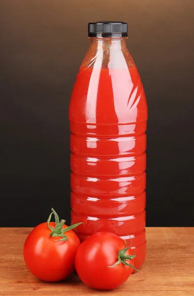 Tomato juice in bottle on wooden table on brown background — Stock Photo, Image