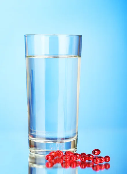 Ein Glas Wasser und Pillen auf blauem Hintergrund in Nahaufnahme — Stockfoto