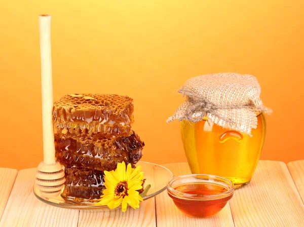 Frasco de mel e favo de mel na mesa de madeira no fundo laranja — Fotografia de Stock