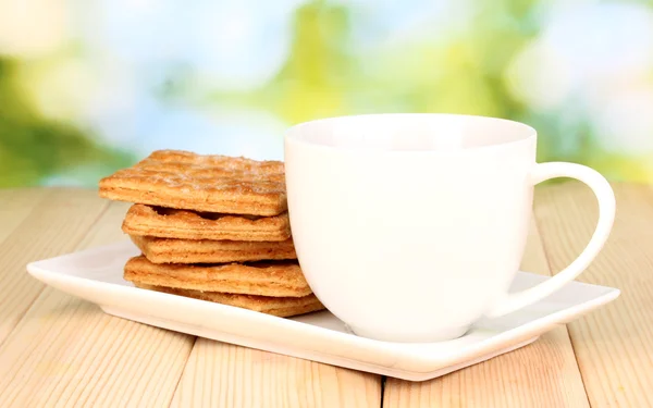 Xícara de chá e biscoitos na mesa de madeira no fundo brilhante — Fotografia de Stock