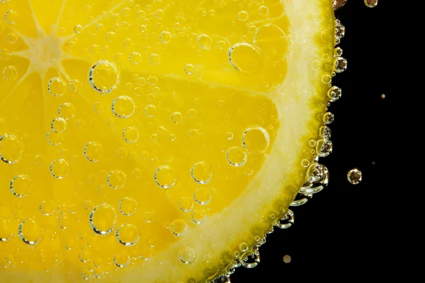 Rebanada de cal en el agua con burbujas, sobre fondo negro — Foto de Stock