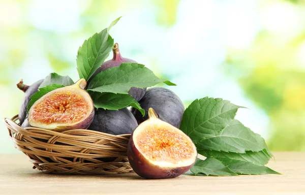 Ripe sweet figs with leaves in basket, on wooden table, on green background — Stock Photo, Image