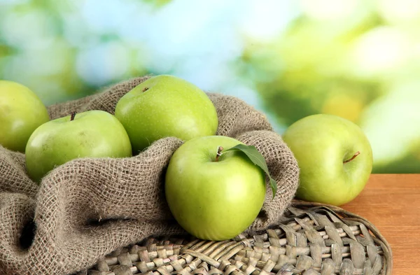 Ripe green apples with leaves on burlap, on wooden table, on green backgrou — Stock Photo, Image