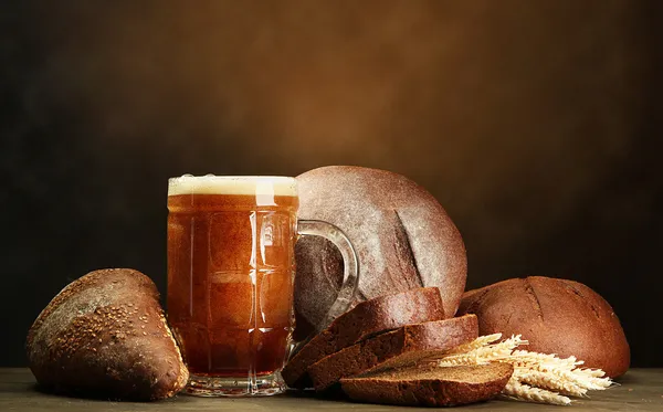 Танкард из кваса и ржаного хлеба с ушами, на деревянном столе на коричневом бэкгро — стоковое фото