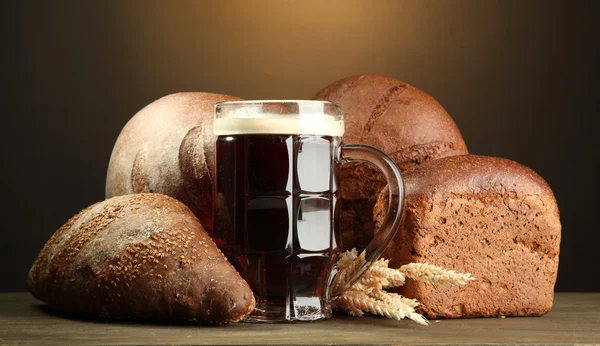Tankard of kvass and rye breads with ears, on wooden table on brown backgro — Stock Photo, Image