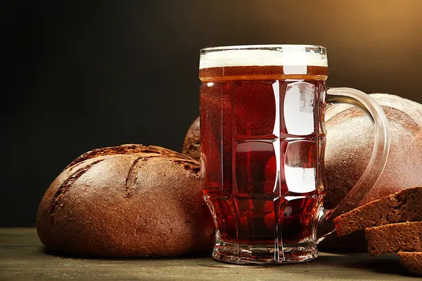 Tankard of kvass and rye breads, on wooden table on brown background — Stock Photo, Image