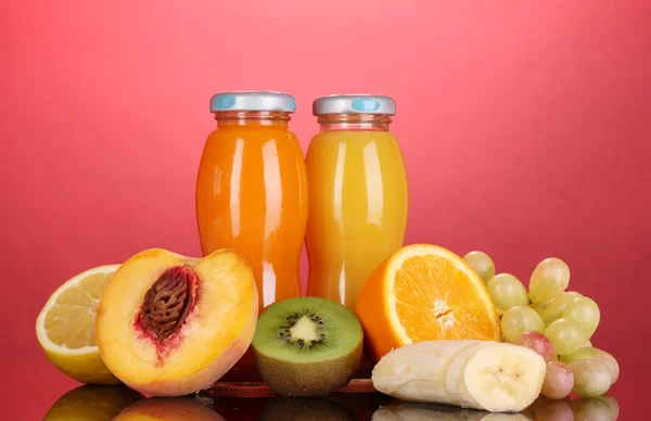 Délicieux jus de multifruit dans une bouteille et des fruits à côté sur fond rose — Photo