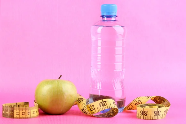 Fles water, apple en meten tape op roze achtergrond — Stockfoto