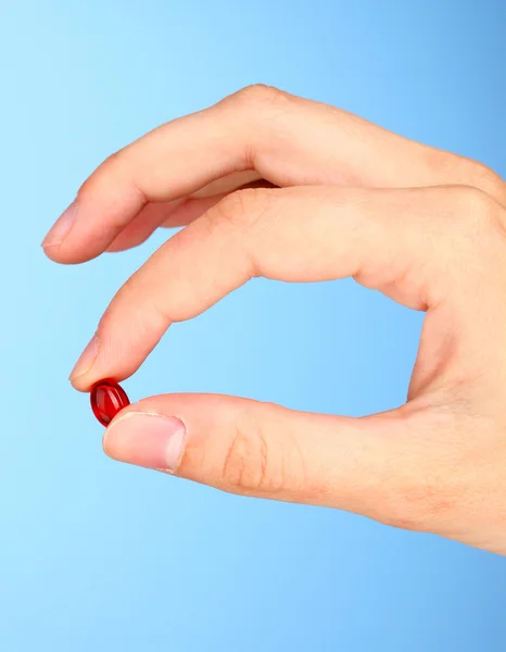 Woman's hand holding a red pill on blue background close-up Stock Image